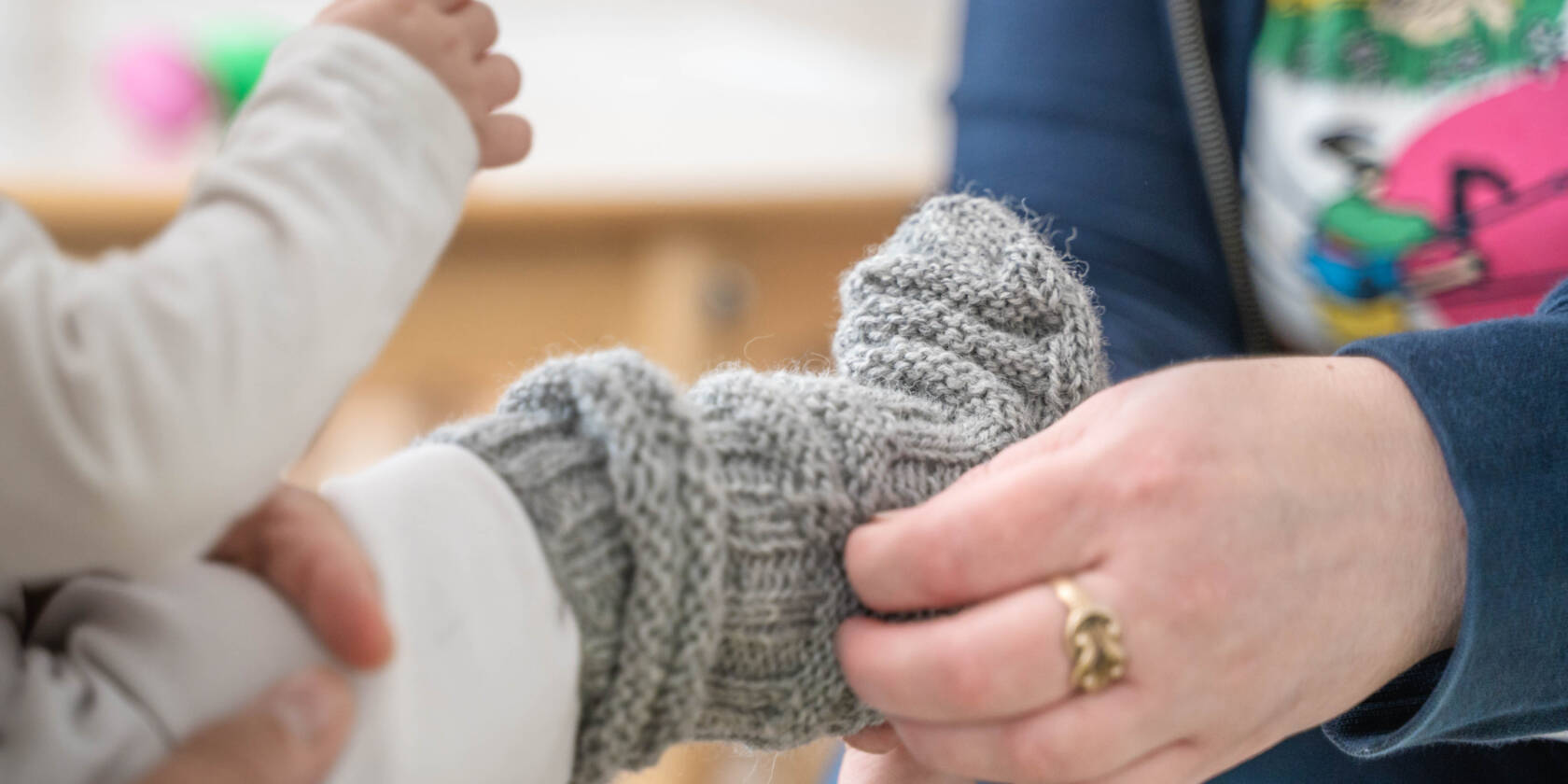Lastenohjaaja laittaa lapselle sukan jalkaan.
