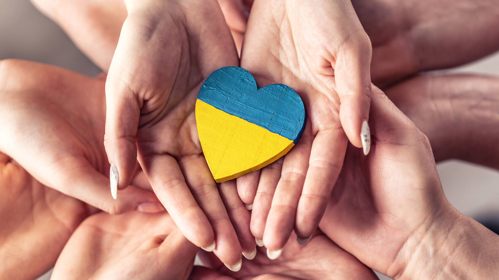 Puinen sydän Ukrainan väreissä useiden käsien pitelemänä.
