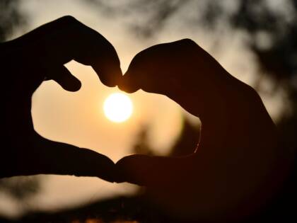 Kädet muodostavat sydämen, jonka keskellä laskeva aurinko.