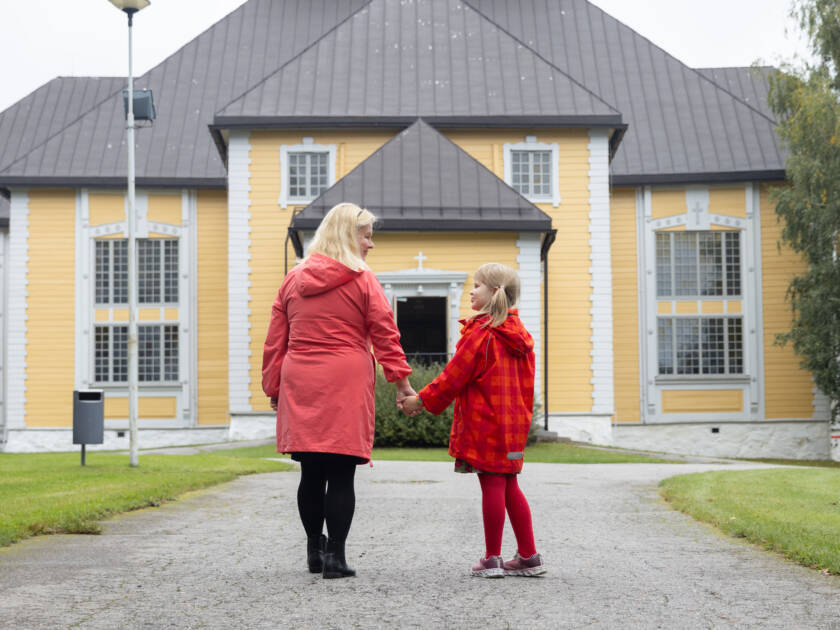 Pieni tyttö pitelee isoäitiä kädestä heidän seisoessaan Mikkelin Pitäjänkirkon edessä.