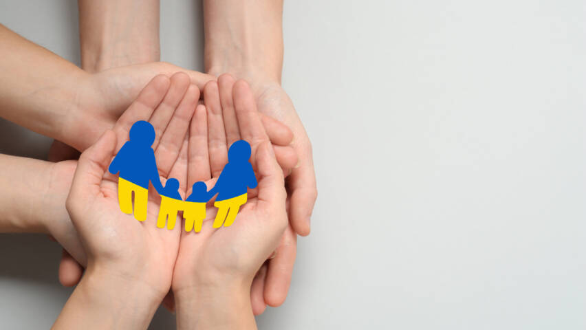Useita käsipareja pitelemässä kämmenellään Ukrainan lipun värisestä paperista leikattuja ihmishahmoja.